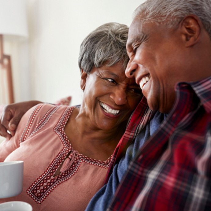 a couple holding coffee mugs and smiling while lounging on a couch