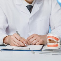 : a dentist writing on a clipboard with a model of a mouth sitting next to them