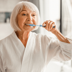older woman with dental implants brushing her teeth