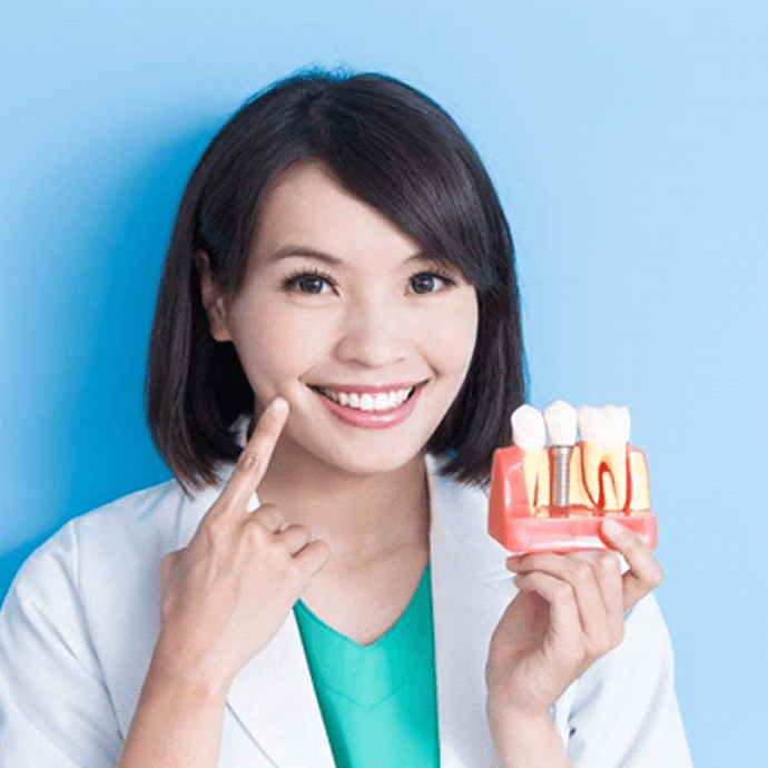 Smiling Longmont implant dentist pointing to smile and holding dental implant model