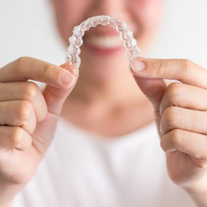 Smiling woman holding out Invisalign in Longmont