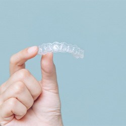 Patient holding up Invisalign aligner against blue background