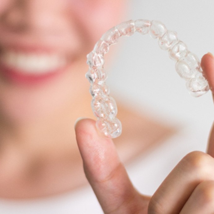 Closeup of smiling woman holding Invisalign aligner