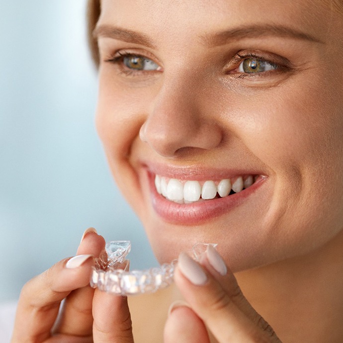 Smiling woman holding out Invisalign in Longmont