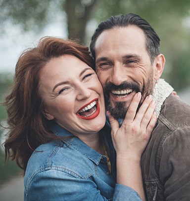 Smiling man and woman with text that reads implant retained dentures all inclusive pricing please call for additional details
