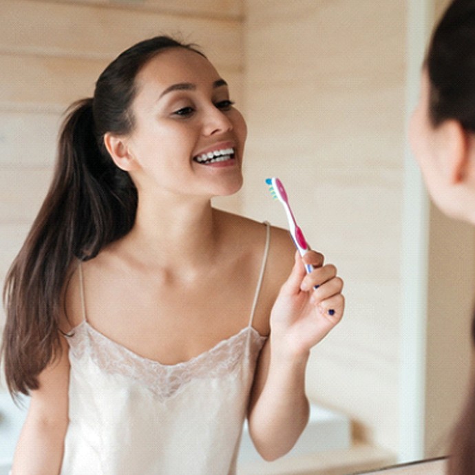 Woman brushing teeth after teeth whitening in Longmont