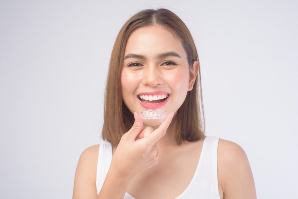 Woman smiling while putting on Invisalign